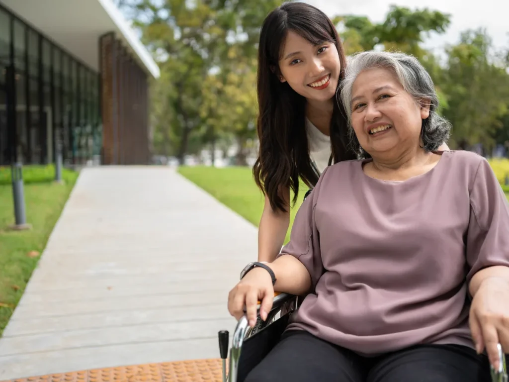 Elderly woman on a wheelchair outside a nursing home accompanied by a female nurse