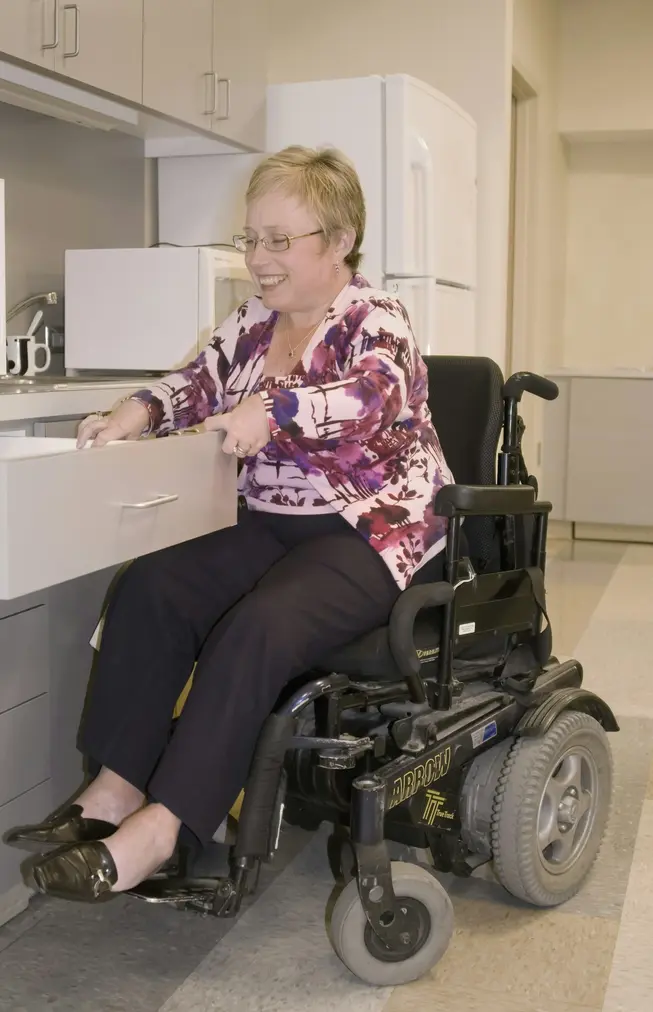 Woman in wheelchair, smiling while opening a drawer in a kitchen