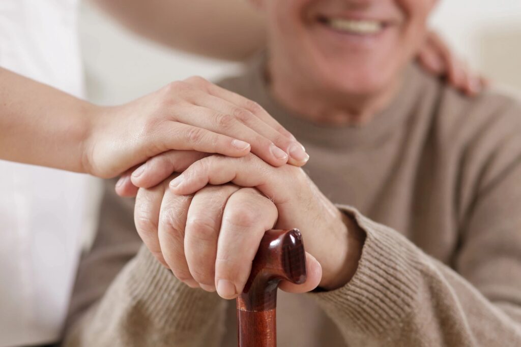 Close-up of hands of elderly person holding a walking cane, with the person in the background, smiling